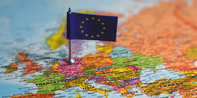 A close-up of a map of Europe featuring a small flag of the European Union positioned over a country.
